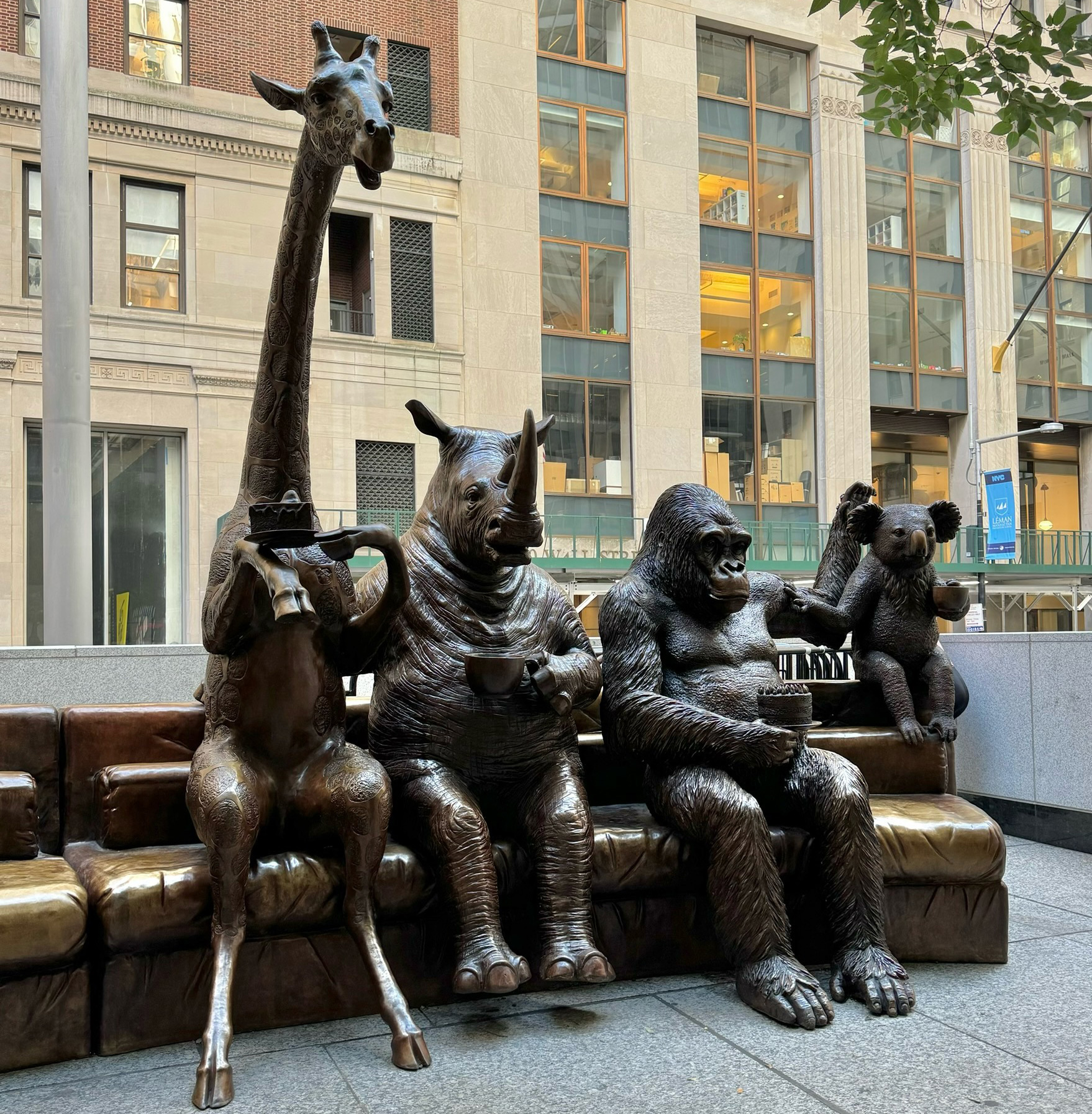 Bronze statue of a family of animals sitting together having tea, on a sofa.