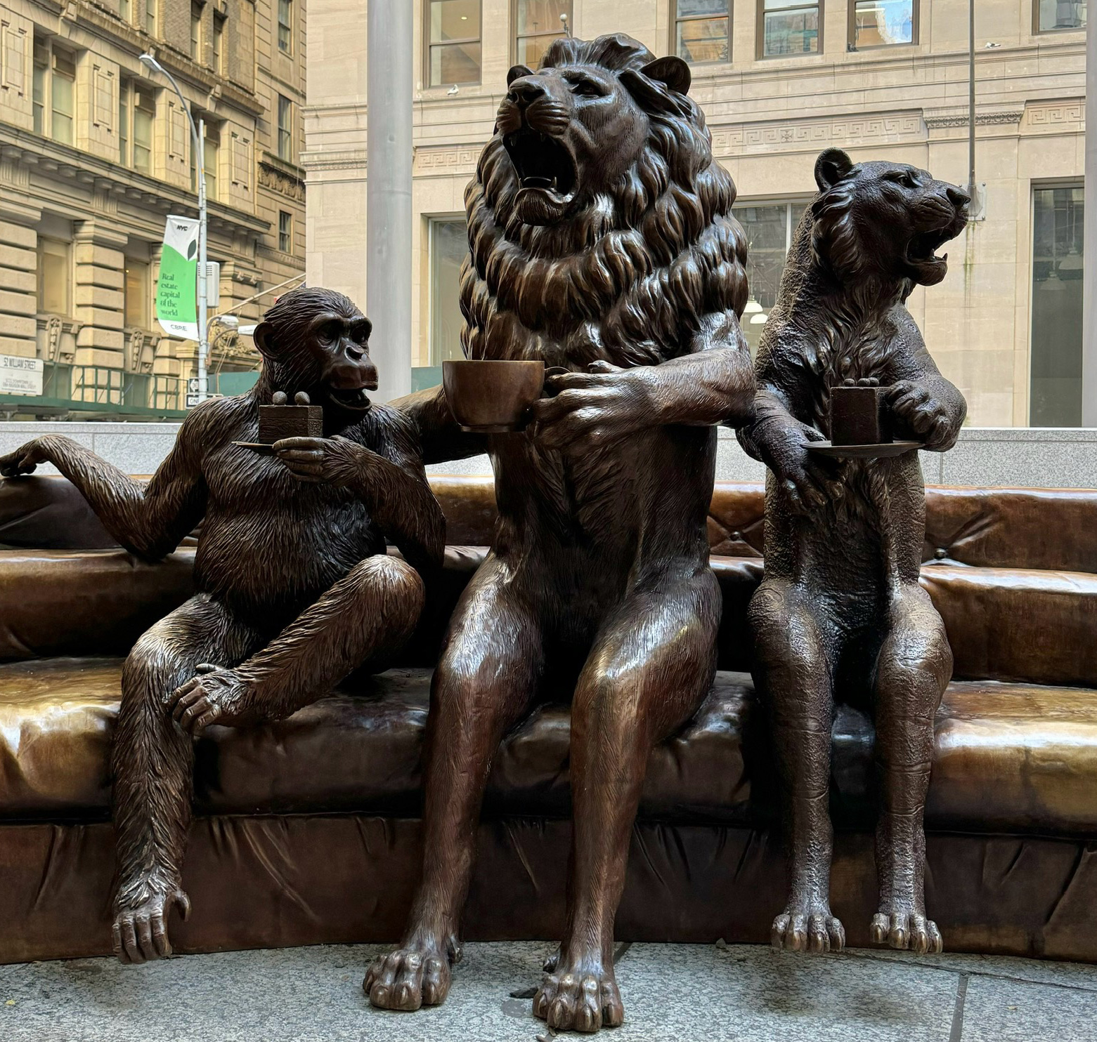 Bronze statue of a family of animals sitting together having tea, on a sofa.